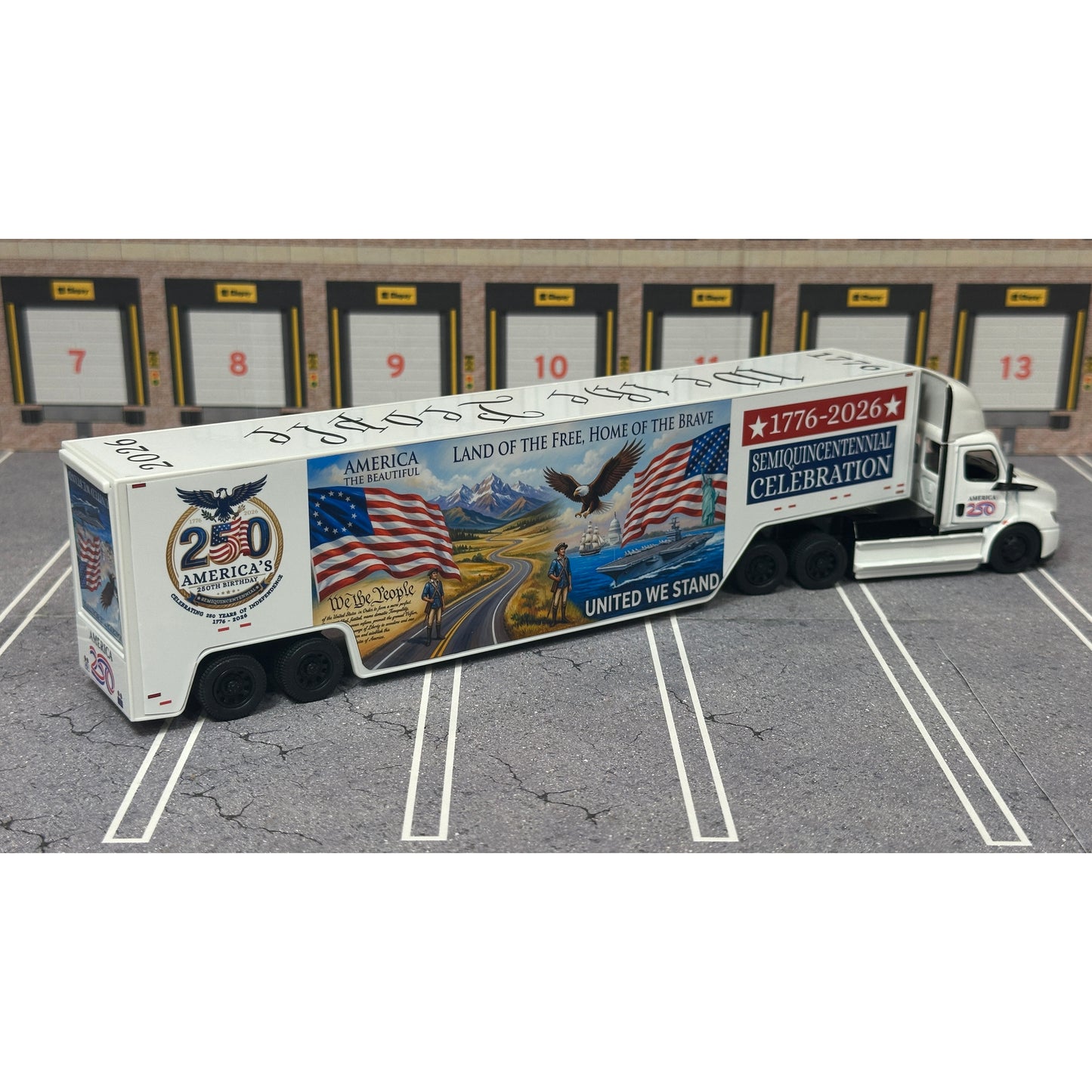 A diecast model of a Freightliner Cascadia semi-truck parked in a simulated parking lot. The trailer features a detailed historical design celebrating the United States' 250th anniversary with 'We the People' written on the top, alongside an American flag, eagle, and city skyline graphic with the text 'Land of the Free Home of the Brave' and 'United We Stand'.
