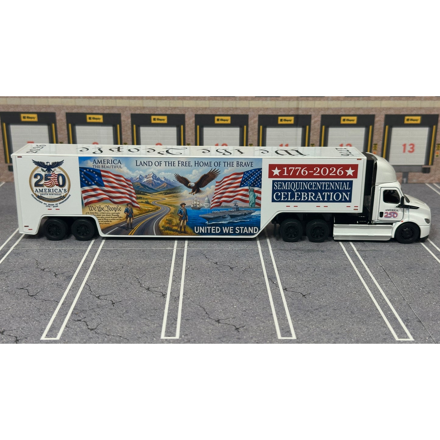 A diecast model of a Freightliner Cascadia semi-truck parked in a simulated parking lot. The trailer features a detailed historical design celebrating the United States' 250th anniversary with 'We the People' written on the top, alongside an American flag, eagle, and city skyline graphic with the text 'Land of the Free Home of the Brave' and 'United We Stand'.