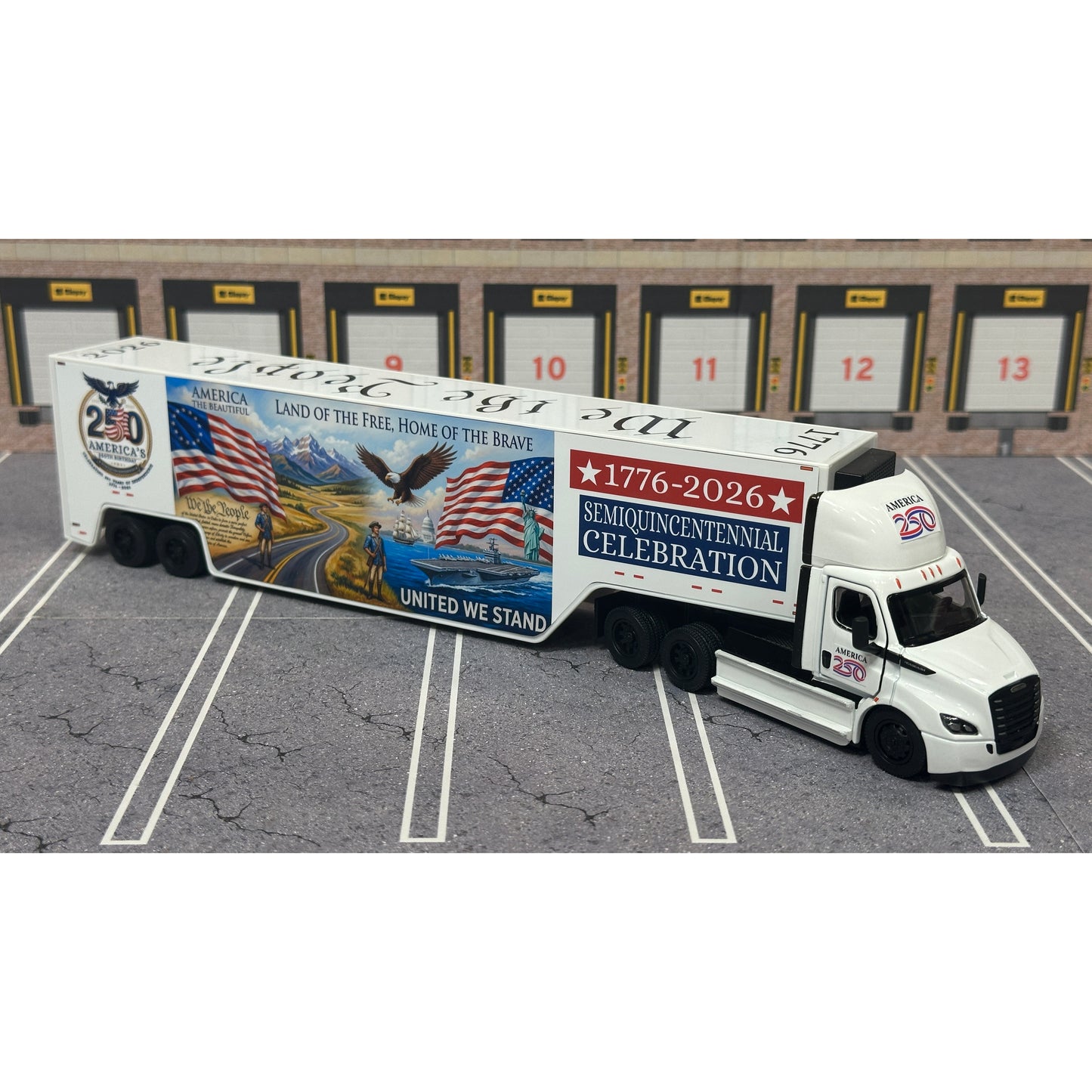 A diecast model of a Freightliner Cascadia semi-truck parked in a simulated parking lot. The trailer features a detailed historical design celebrating the United States' 250th anniversary with 'We the People' written on the top, alongside an American flag, eagle, and city skyline graphic with the text 'Land of the Free Home of the Brave' and 'United We Stand'.