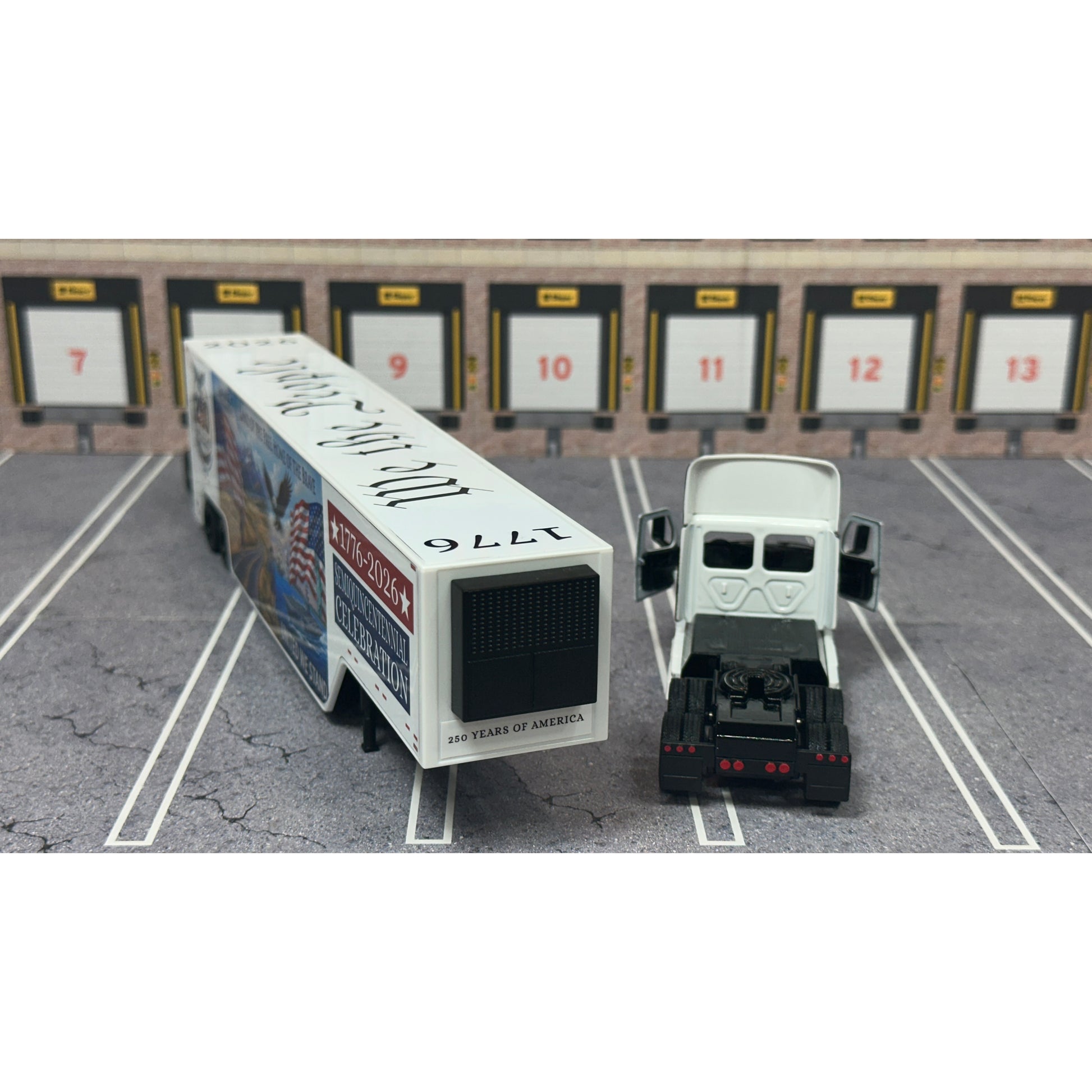 A diecast model of a Freightliner Cascadia semi-truck parked in a simulated parking lot. The trailer features a detailed historical design celebrating the United States' 250th anniversary with 'We the People' written on the top, alongside an American flag, eagle, and city skyline graphic with the text 'Land of the Free Home of the Brave' and 'United We Stand'.