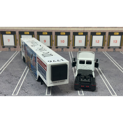 A diecast model of a Freightliner Cascadia semi-truck parked in a simulated parking lot. The trailer features a detailed historical design celebrating the United States' 250th anniversary with 'We the People' written on the top, alongside an American flag, eagle, and city skyline graphic with the text 'Land of the Free Home of the Brave' and 'United We Stand'.