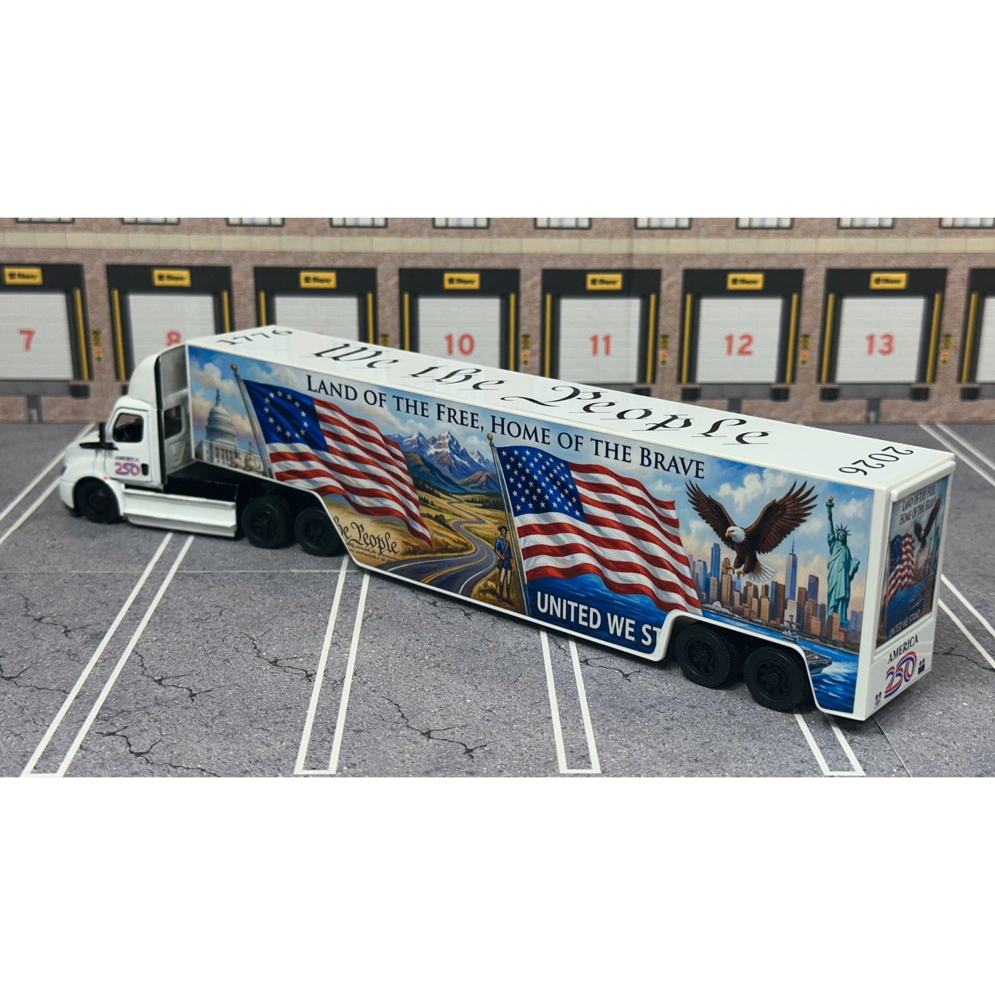 A diecast model of a Freightliner Cascadia semi-truck parked in a simulated parking lot. The trailer features a detailed historical design celebrating the United States' 250th anniversary with 'We the People' written on the top, alongside an American flag, eagle, and city skyline graphic with the text 'Land of the Free Home of the Brave' and 'United We Stand'.