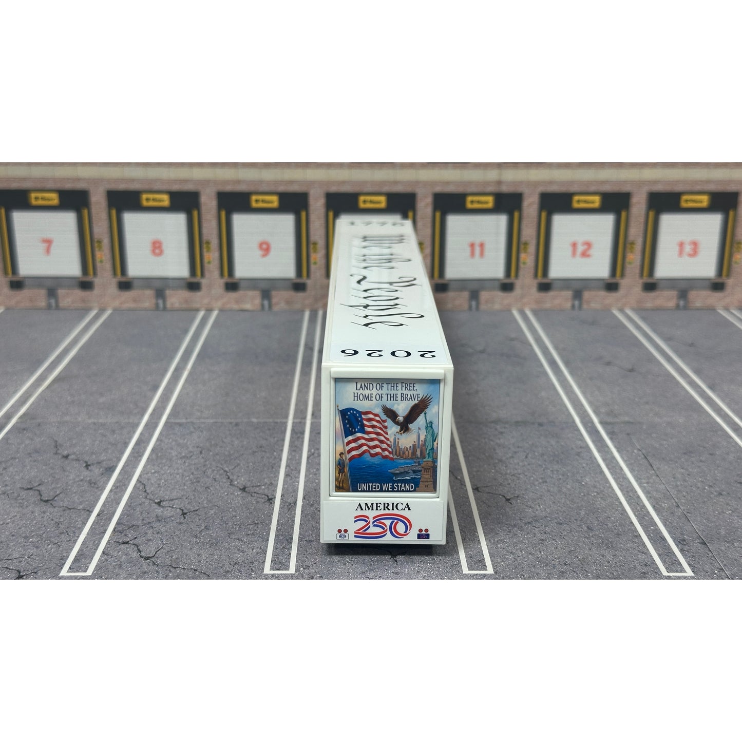 A diecast model of a Freightliner Cascadia semi-truck parked in a simulated parking lot. The trailer features a detailed historical design celebrating the United States' 250th anniversary with 'We the People' written on the top, alongside an American flag, eagle, and city skyline graphic with the text 'Land of the Free Home of the Brave' and 'United We Stand'.