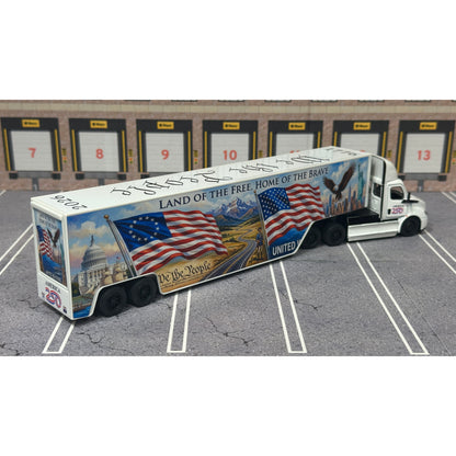 A diecast model of a Freightliner Cascadia semi-truck parked in a simulated parking lot. The trailer features a detailed historical design celebrating the United States' 250th anniversary with 'We the People' written on the top, alongside an American flag, eagle, and city skyline graphic with the text 'Land of the Free Home of the Brave' and 'United We Stand'.