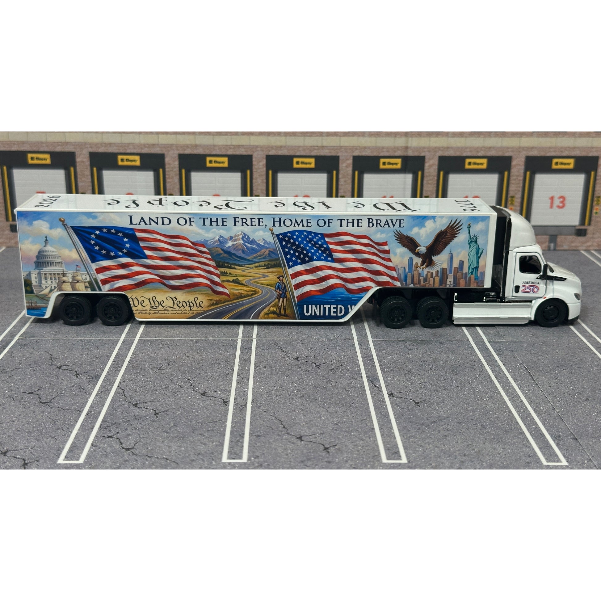 A diecast model of a Freightliner Cascadia semi-truck parked in a simulated parking lot. The trailer features a detailed historical design celebrating the United States' 250th anniversary with 'We the People' written on the top, alongside an American flag, eagle, and city skyline graphic with the text 'Land of the Free Home of the Brave' and 'United We Stand'.