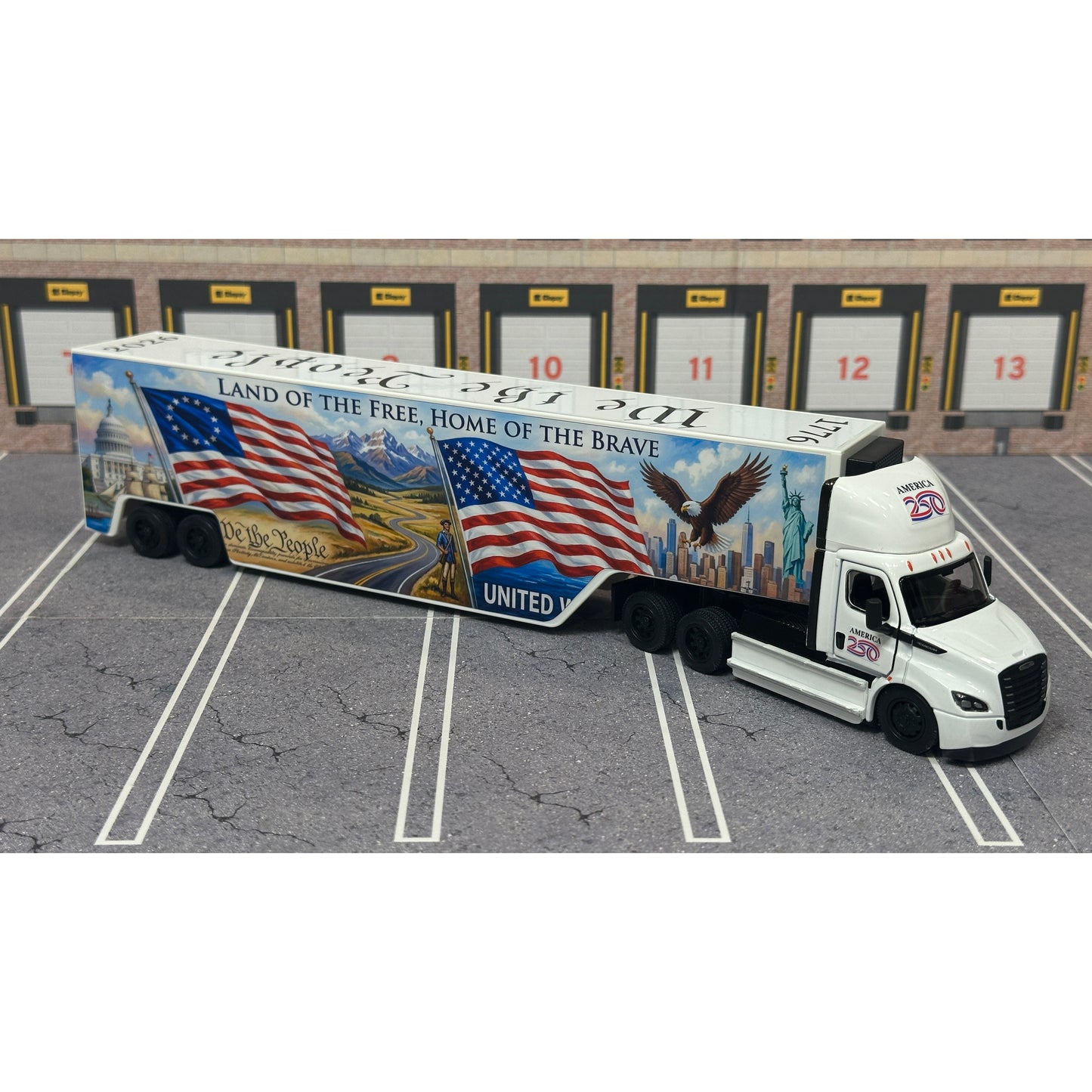 A diecast model of a Freightliner Cascadia semi-truck parked in a simulated parking lot. The trailer features a detailed historical design celebrating the United States' 250th anniversary with 'We the People' written on the top, alongside an American flag, eagle, and city skyline graphic with the text 'Land of the Free Home of the Brave' and 'United We Stand'.