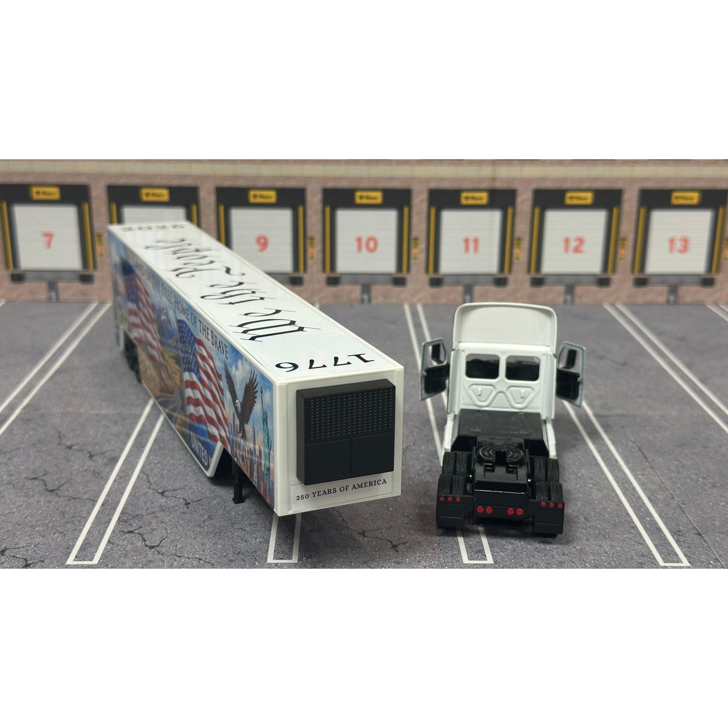 A diecast model of a Freightliner Cascadia semi-truck parked in a simulated parking lot. The trailer features a detailed historical design celebrating the United States' 250th anniversary with 'We the People' written on the top, alongside an American flag, eagle, and city skyline graphic with the text 'Land of the Free Home of the Brave' and 'United We Stand'.