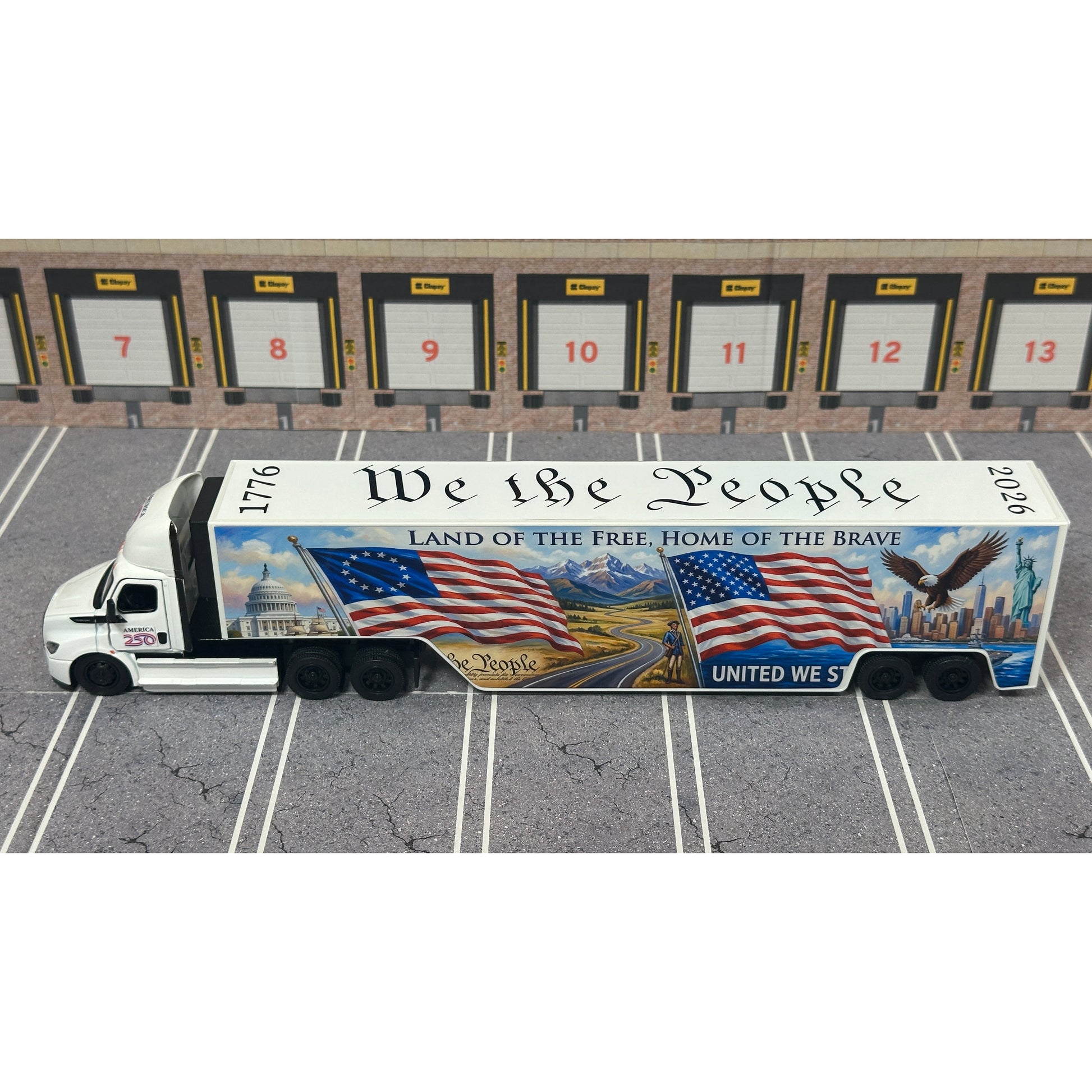 A diecast model of a Freightliner Cascadia semi-truck parked in a simulated parking lot. The trailer features a detailed historical design celebrating the United States' 250th anniversary with 'We the People' written on the top, alongside an American flag, eagle, and city skyline graphic with the text 'Land of the Free Home of the Brave' and 'United We Stand'.