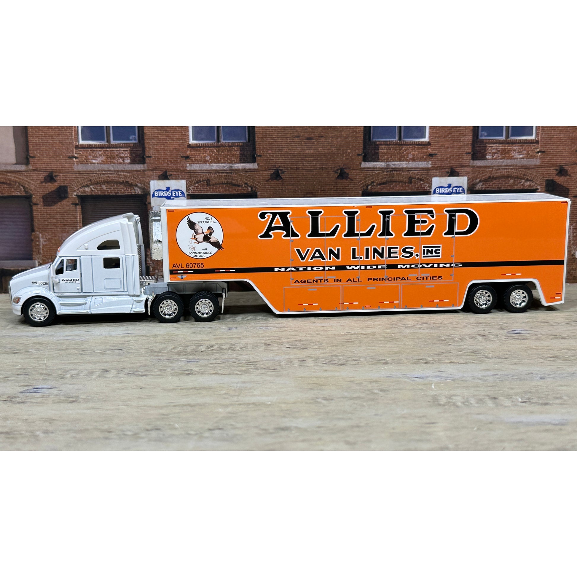 Model of a moving truck with 'Allied Van Lines' branding in front of a brick building.