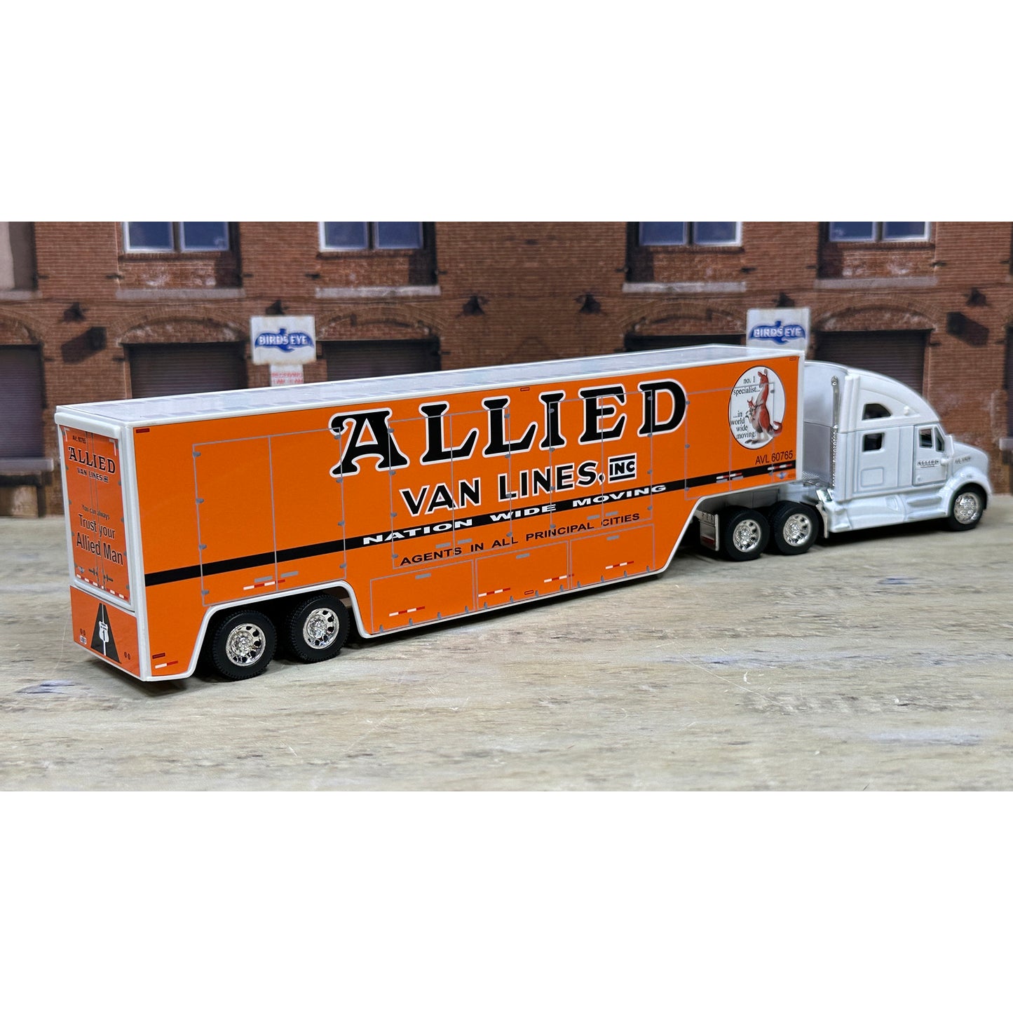 Model of a semi-truck with 'Allied Van Lines' branding in front of a brick building.