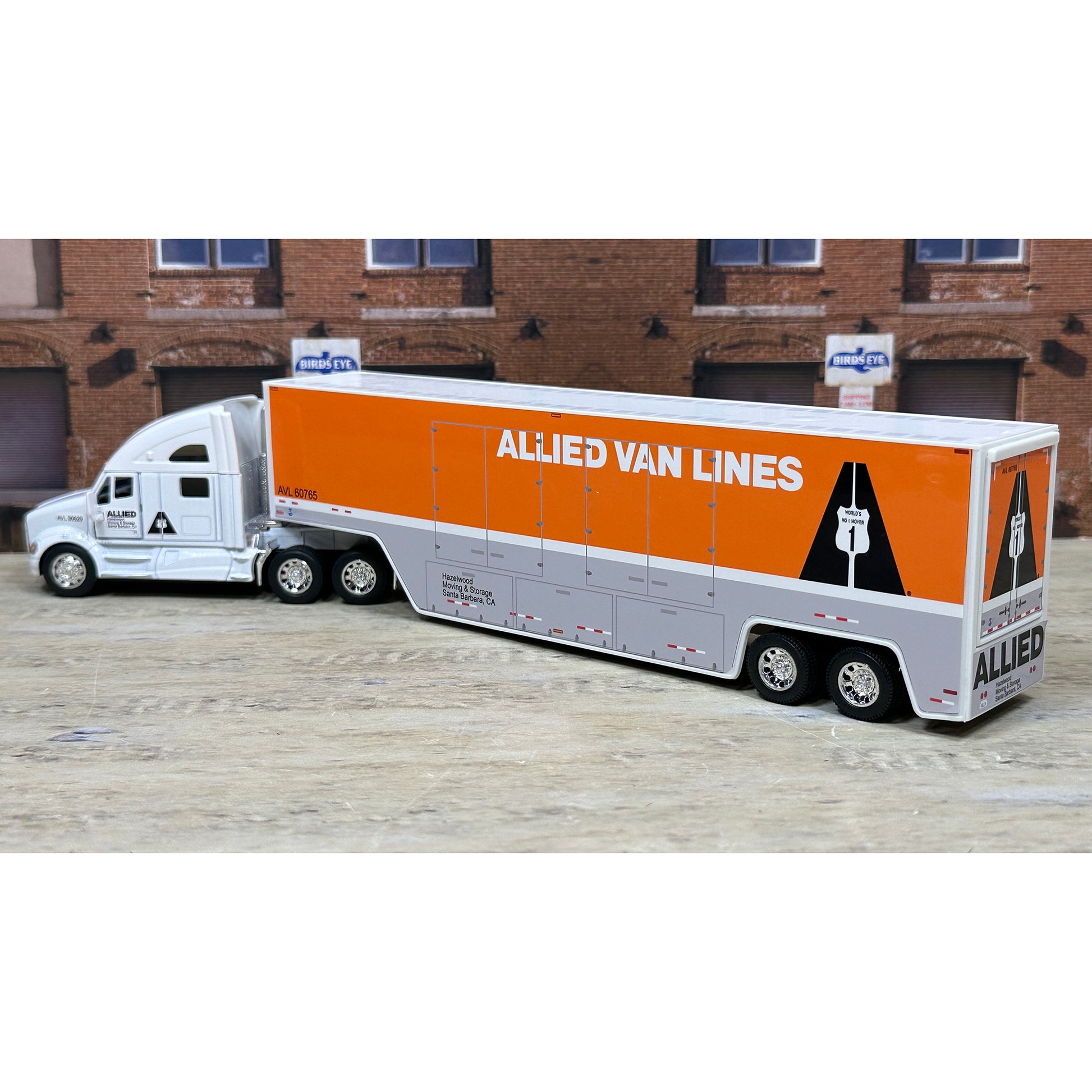Model of a semi-truck with an orange trailer labeled 'Allied Van Lines' in front of a brick building.