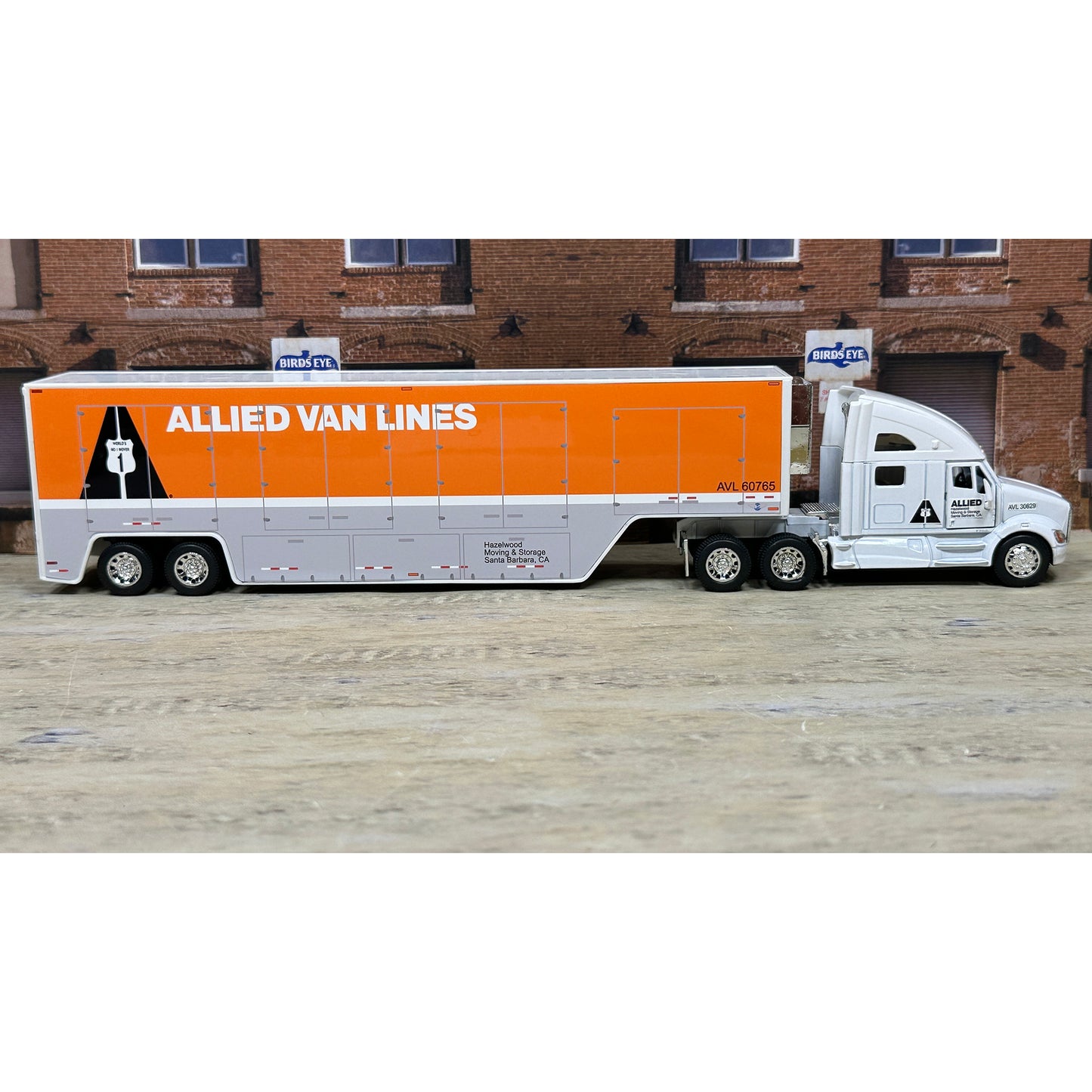 Model of a truck with 'Allied Van Lines' branding in front of a brick building.