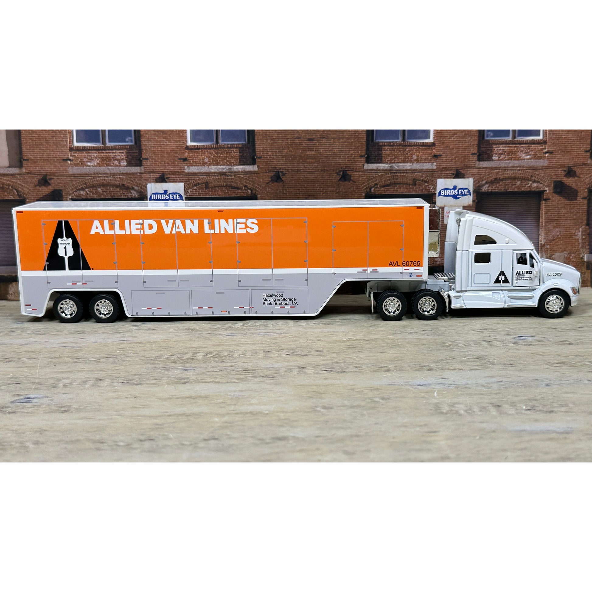 Model of a truck with 'Allied Van Lines' branding in front of a brick building.