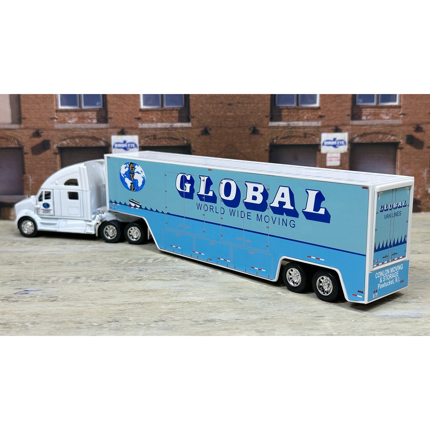 Model of a Global World Wide Moving truck in front of a brick building.