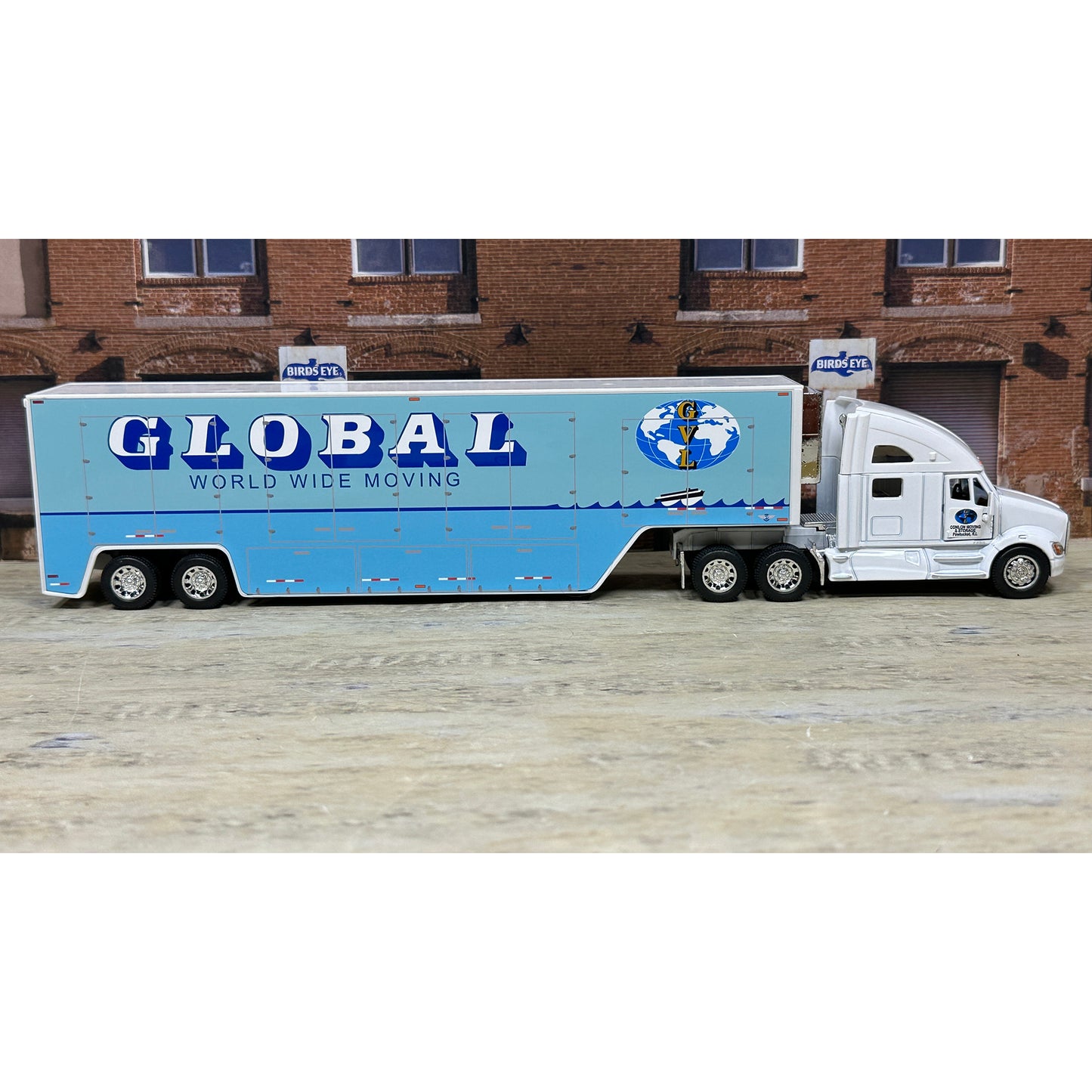 Model truck with 'Global World Wide Moving' trailer in front of a brick building.
